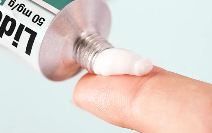 Anwendung von Lidoproct und Dosierung Nahaufnahme eines Zeigefinger, auf den Salbe aus einer Lidoproct Tube gedrückt wird