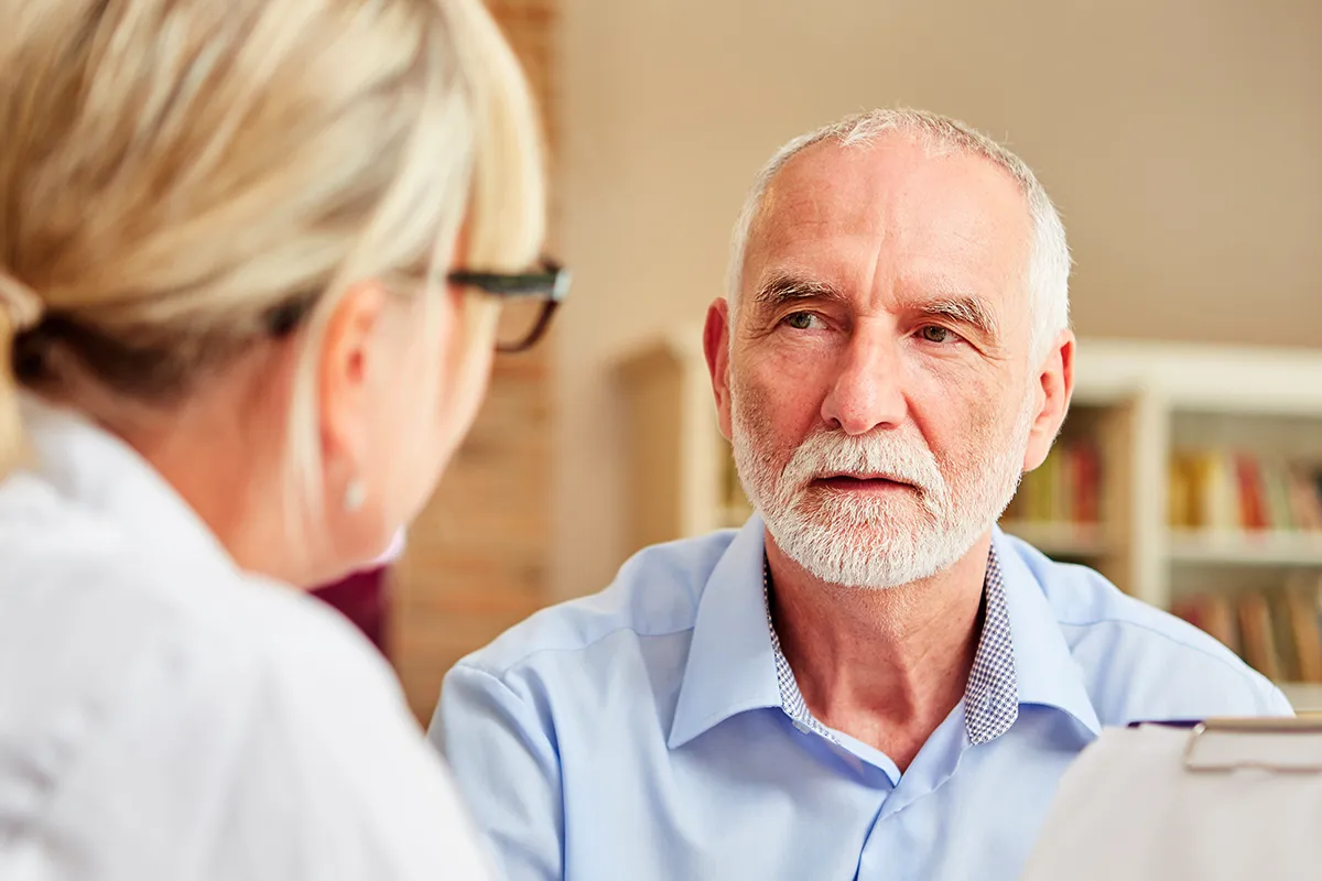 Eine weibliche Person mit Klemmbrett und Kugelschreiber in der Hand, sitz vor einer älteren männlichen Person