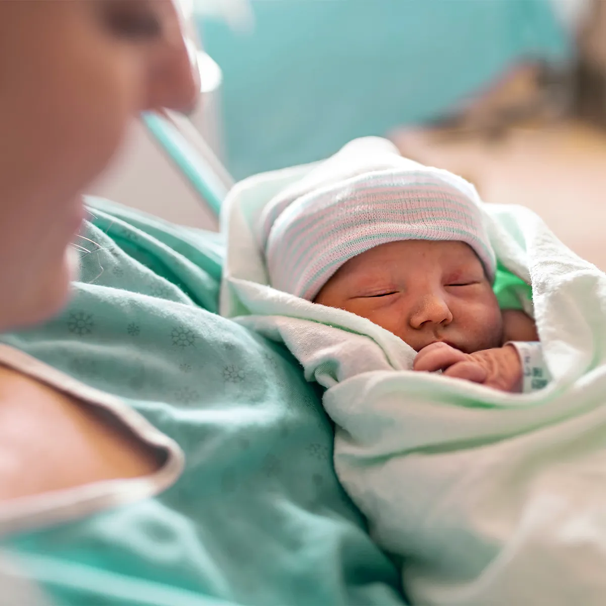 Eine weibliche Person hält ein kleines, in Tücher eingewickeltes Baby mit Mütze im Arm.