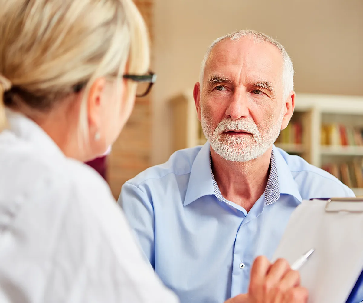 entzuendungen-im-analbereich-behandlungsformen Eine weibliche Person mit Klemmbrett und Kugelschreiber in der Hand, sitz vor einer älteren männlichen Person