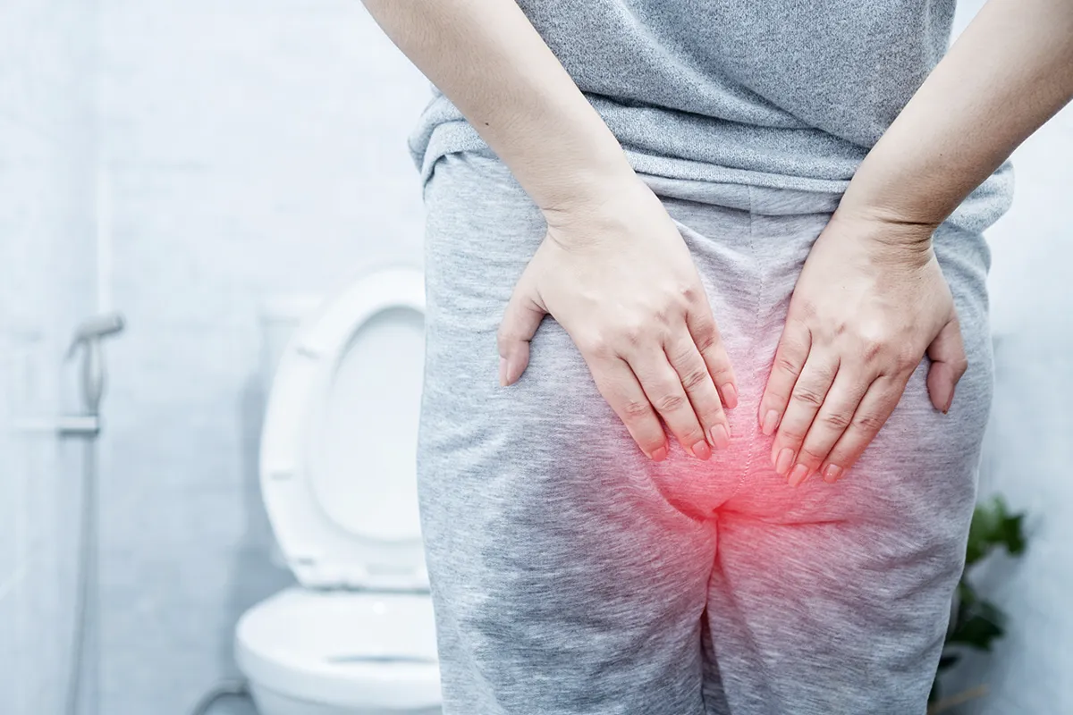 Eine weibliche Person in Jogginanzug vor einer Toilette stehend, mit schemenhaften roten Afterbereich und Händen davor