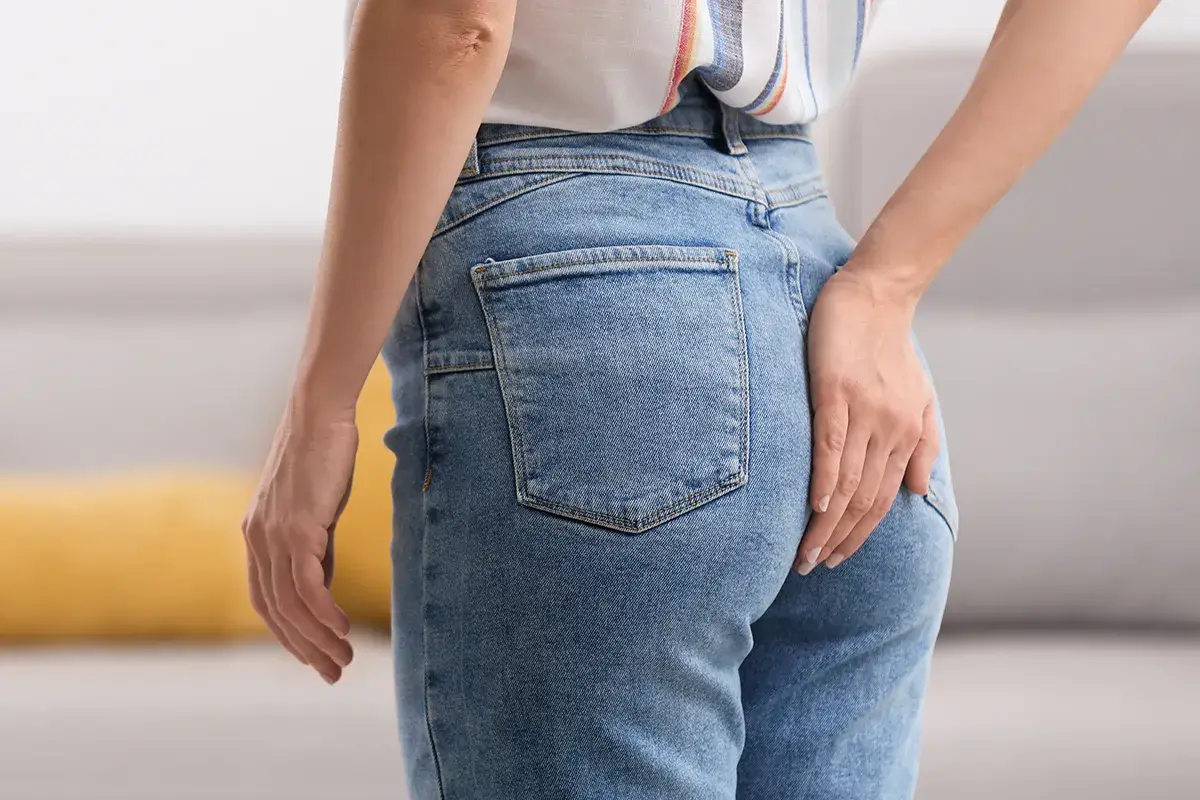 Eine weibliche Person im Profil hält ich die rechte Hand in der Höhe Ihrer Jeanshosentasche auf das Gesäß