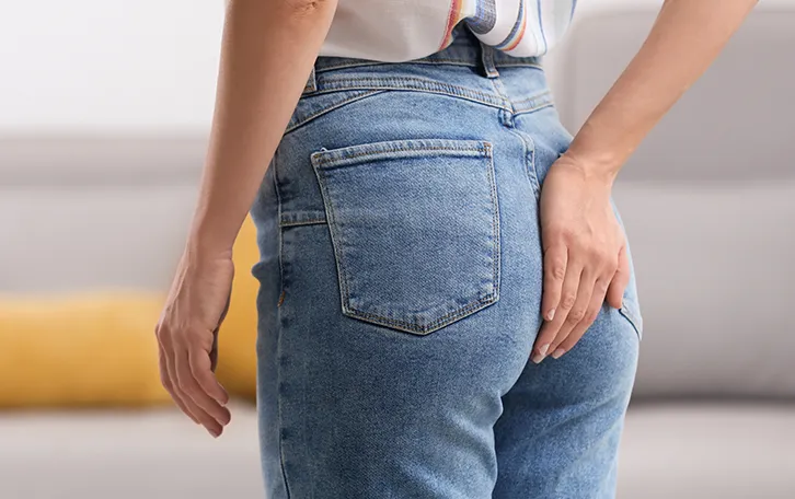 Eine weibliche Person im Profil hält ich die rechte Hand in der Höhe Ihrer Jeanshosentasche auf das Gesäß