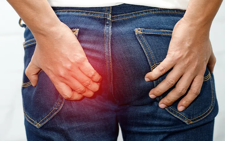 Eine männliche Person hält sich sehr verkrampft mit der linken Hand die linke Pobacke. Schemenhaft ist der Bereich rot überlagert