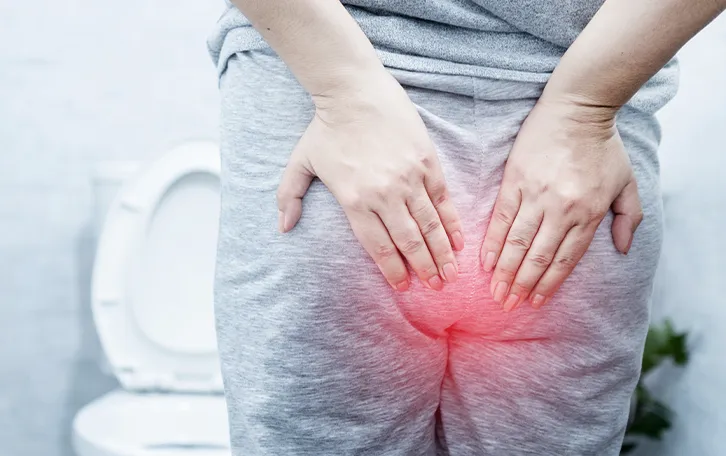 Ratgeber zur Analgesundheit Eine weibliche Person in Jogginanzug vor einer Toilette stehend, mit schemenhaften roten Afterbereich und Händen davor