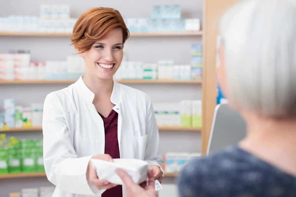 Rektalsalbe Verträglichkeit und Nebenwirkungen Eine Apothekerin übergibt einer Kundin ein Paket über den Tresen