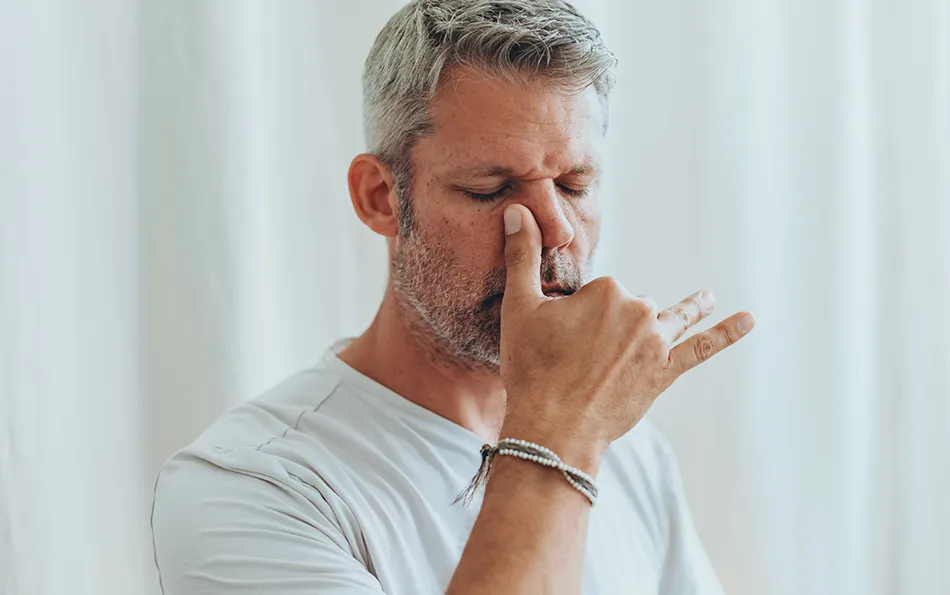 Eine männliche Person mit geschlossenen Augen, die sich den rechten Nasenflügel zu hält