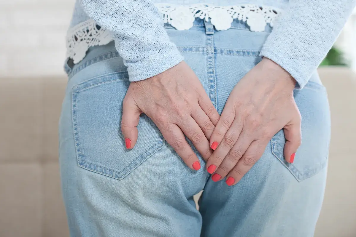 Salbe für den After effektive Lösung Eine Person hält sich beide Hände in der Höhe Ihrer Jeanshosentaschen auf das Gesäß