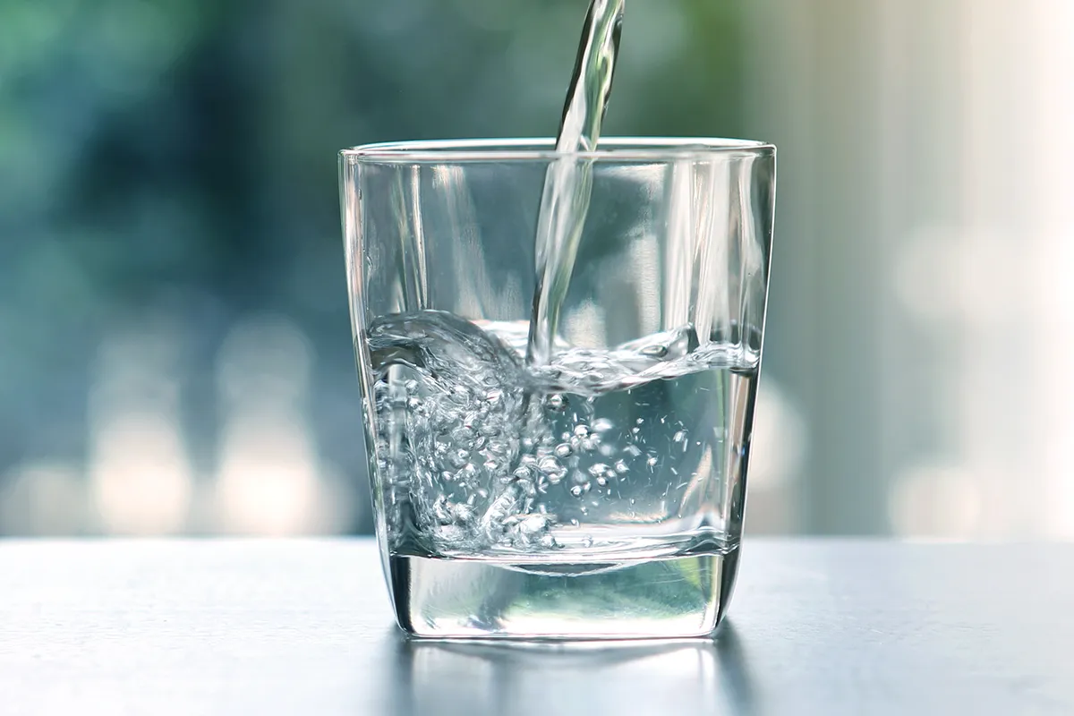 Schmerzen beim Stuhlgang gute Flüssigkeitszufuhr Wasser wird in ein Glas gekippt