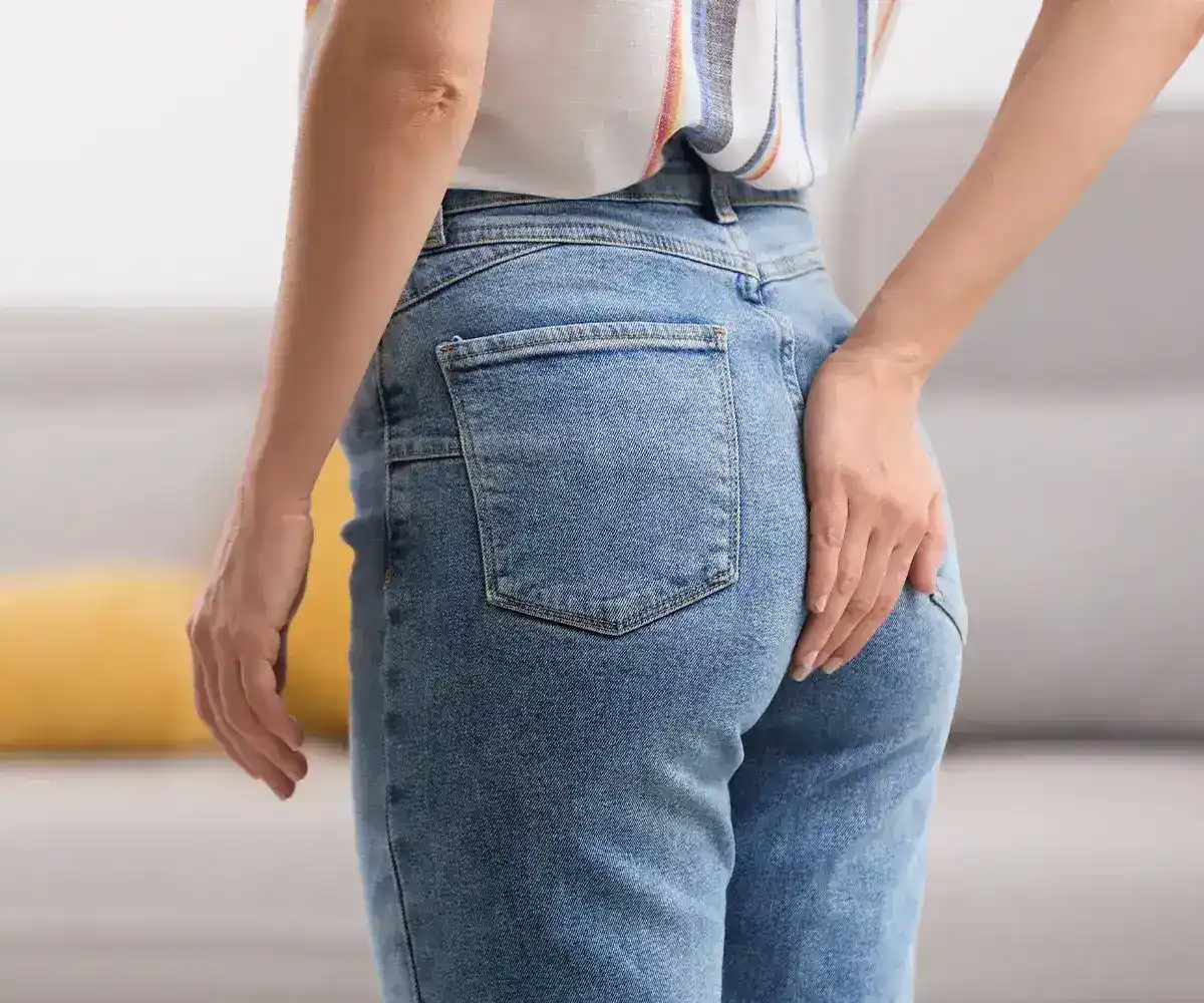 Schmerzen beim Stuhlgang Lidoproct lokale Betäubung Eine weibliche Person im Profil hält ich die rechte Hand in der Höhe Ihrer Jeanshosentasche auf das Gesäß