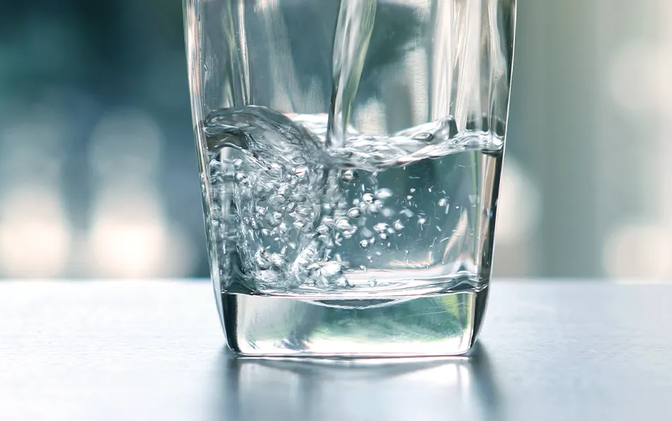 Schmerzen beim Stuhlgang reduzieren ausreichend trinken Wasser wird in ein Glas gekippt