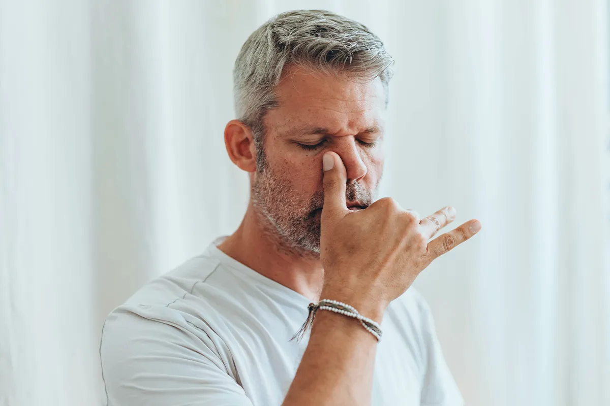 Schmerzen beim Stuhlgang Stressmanagement Eine männliche Person mit geschlossenen Augen, die sich den rechten Nasenflügel zu hält
