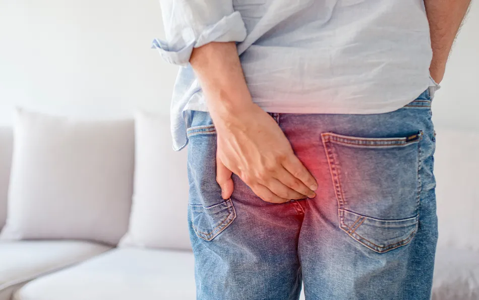 Eine männliche Person hält sich mit der linken Hand den Afterbereich. Schemenhaft ist der Bereich rot überlagert