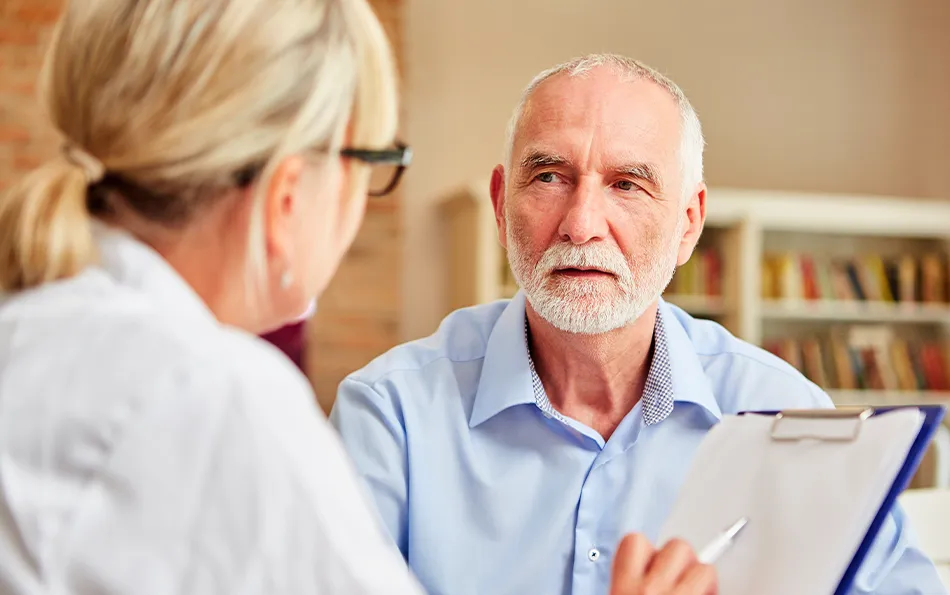 Eine weibliche Person mit Klemmbrett und Kugelschreiber in der Hand, sitz vor einer älteren männlichen Person