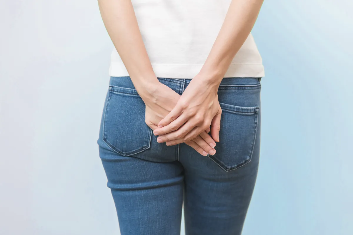 Symptome und Auswirkungen von Afterjucken Eine Person hält sich beide Hände in der Höhe Ihrer Jeanshosentaschen auf das Gesäß