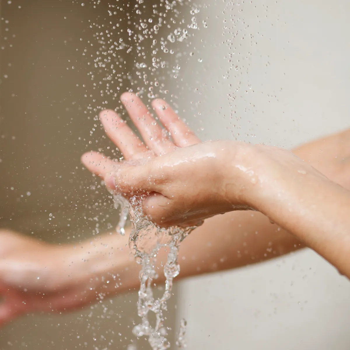 Eine Person unter der Dusche testet mit der einen Hand wie warm das Wasser von oben kommend ist