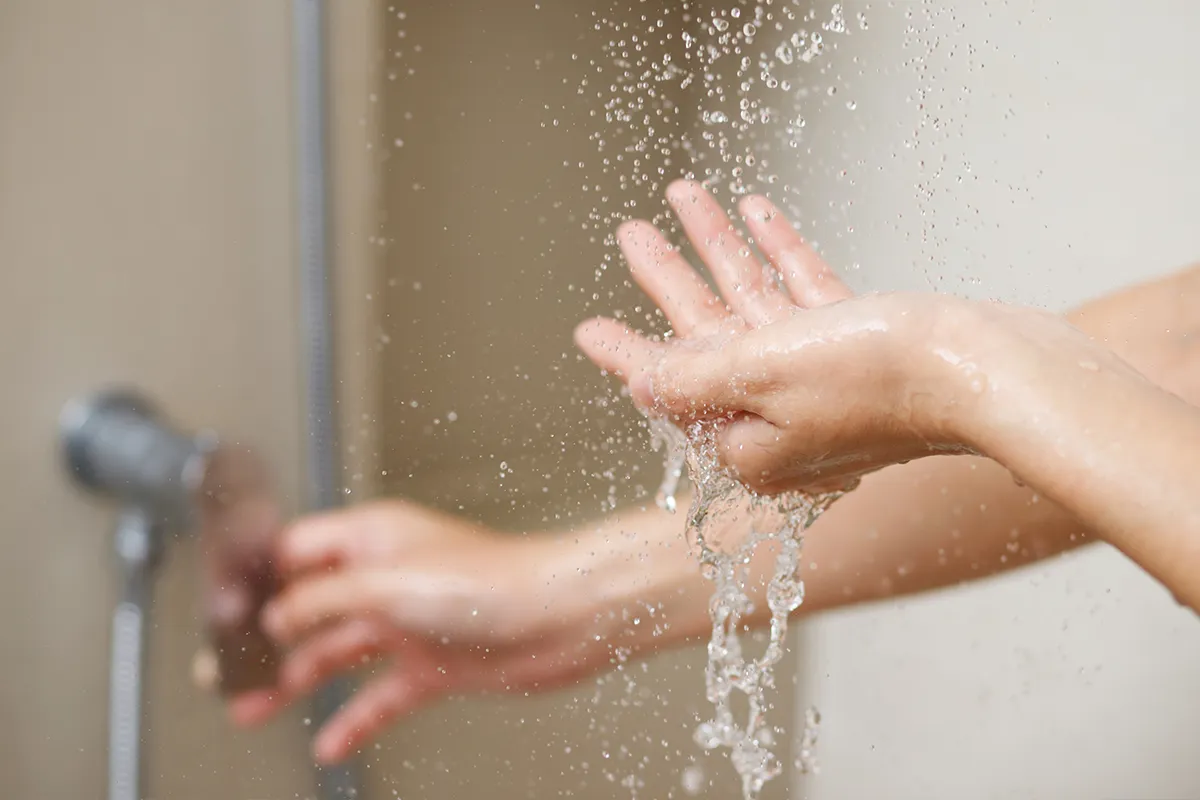 Ursachen für Afterjucken Eine Person unter der Dusche testet mit der einen Hand wie warm das Wasser von oben kommend ist